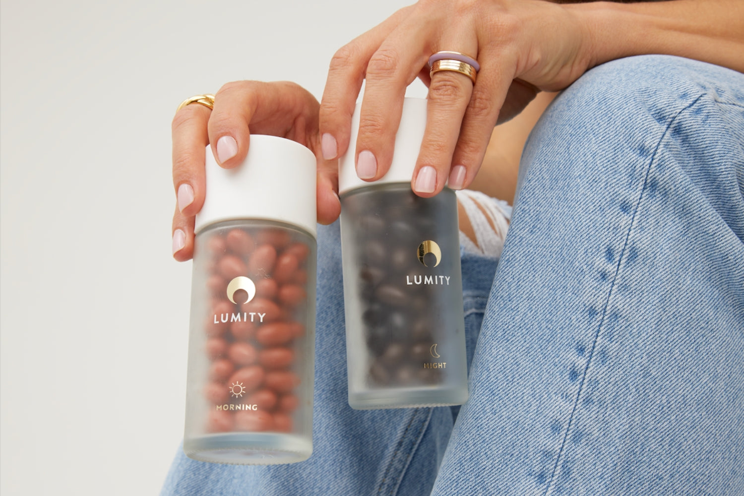Hands holding two frosted Lumity bottles labeled Morning and Night with dark and red supplements inside