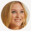 Smiling blonde woman with loose waves looking to the side against a neutral background