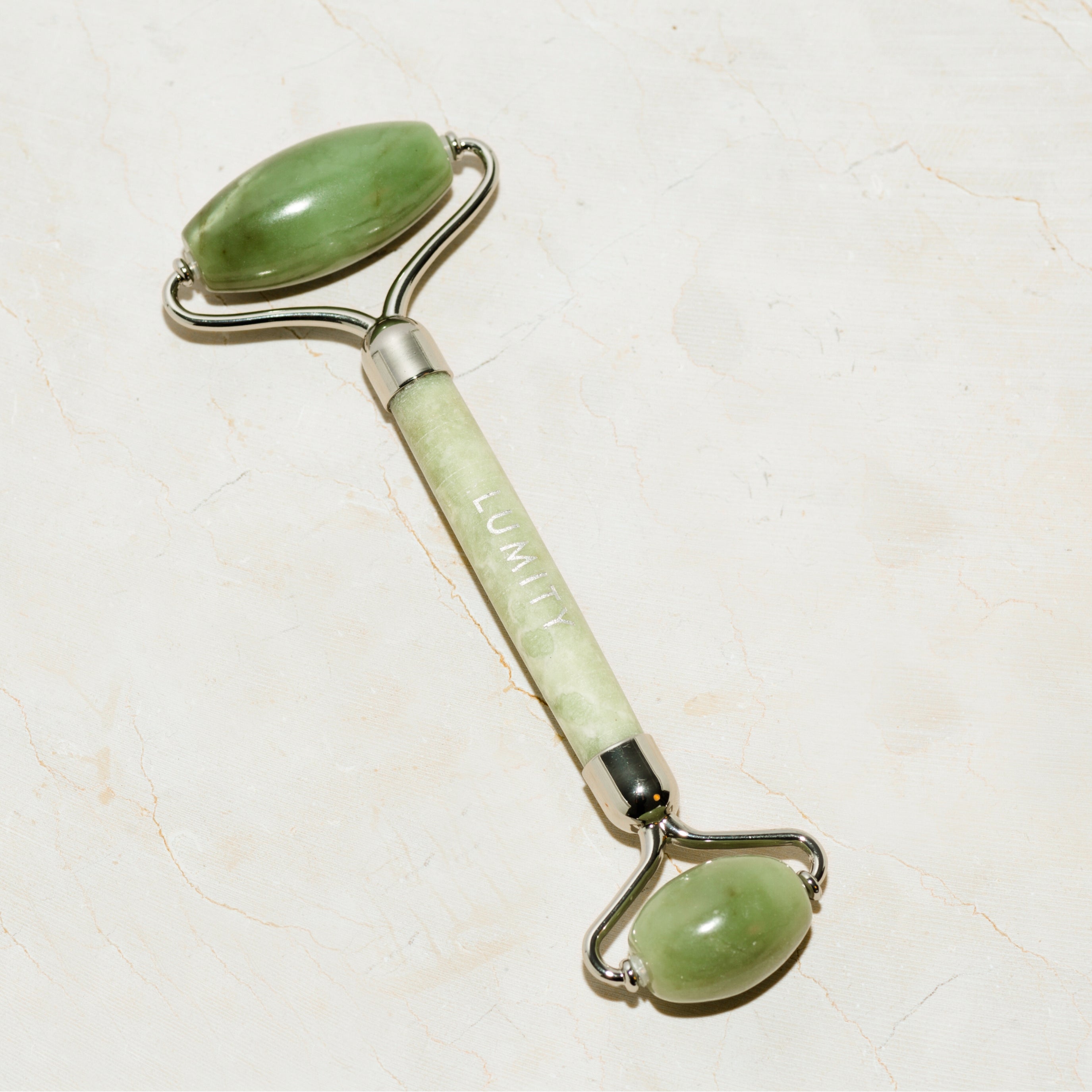 Green jade roller on a light marble background