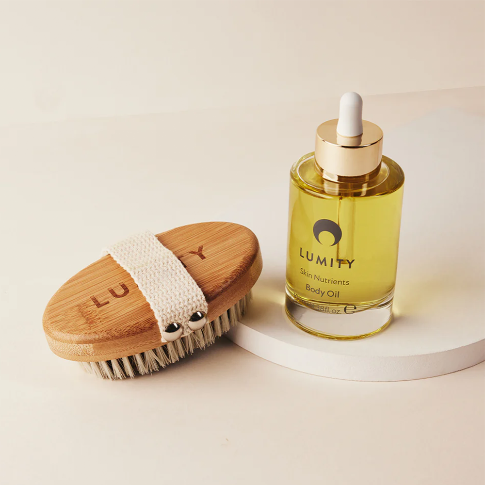 Lumity Skin Nutrients Body Oil bottle and Lumity Copper Body Brush on a light background