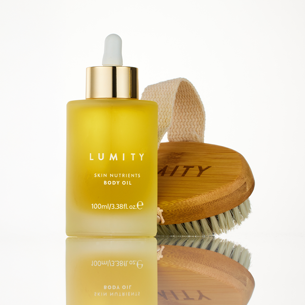Lumity Skin Nutrients Body Oil bottle and Lumity Copper Body Brush on a light background