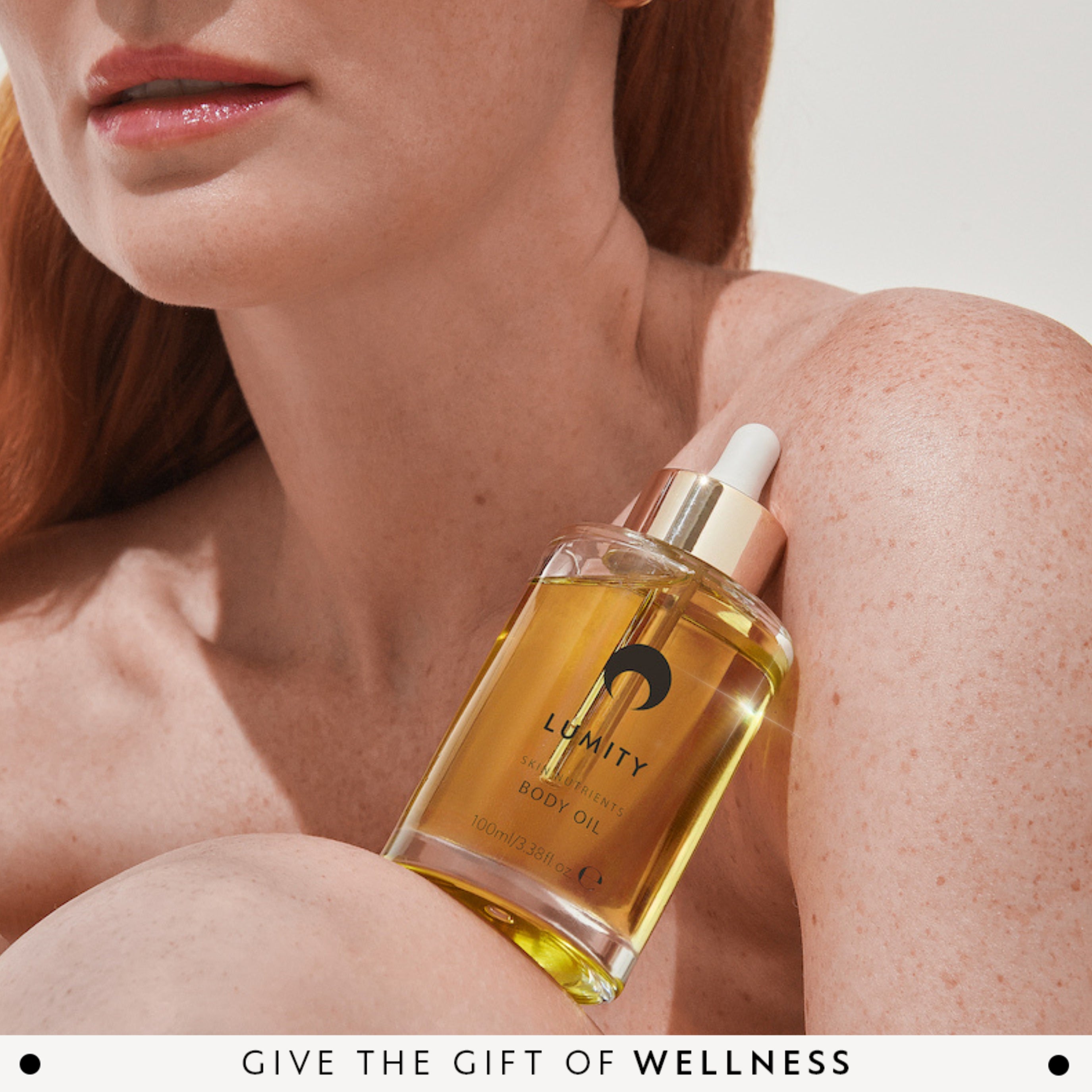 Woman holding a bottle of Lumity body oil with a neutral background