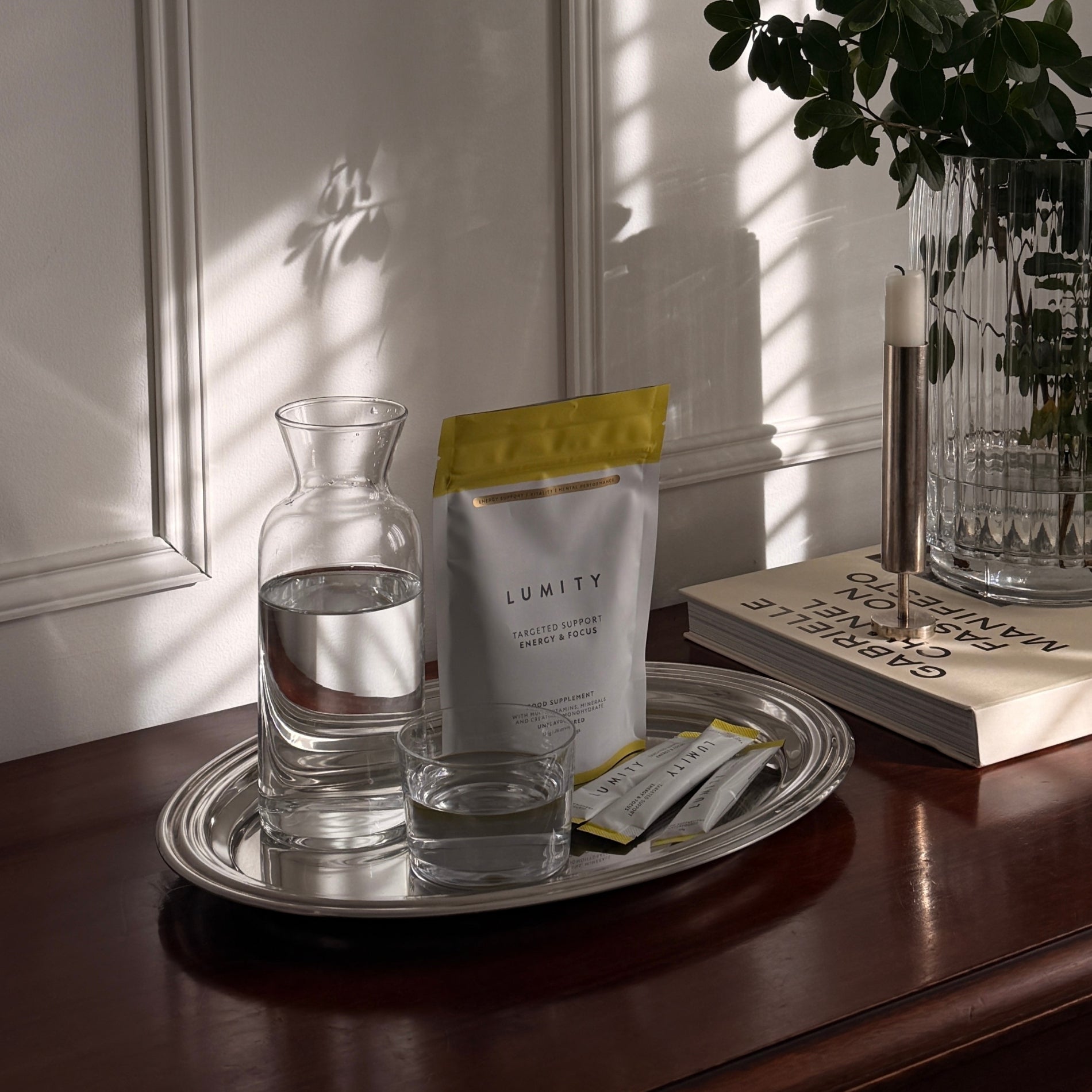 Matte pouch with yellow top and single-serve sticks arranged on a tray with glass and carafe of water by sunlight.