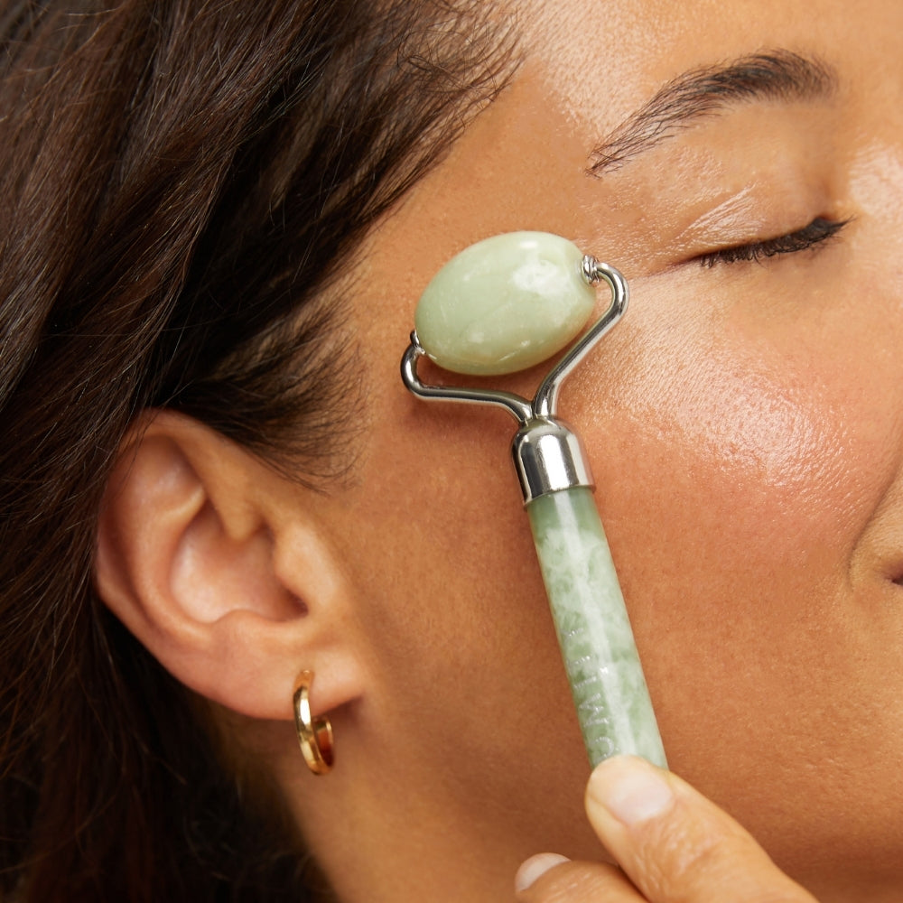Person using a jade roller on their face with text 'Give the Gift of Wellness' at the bottom.