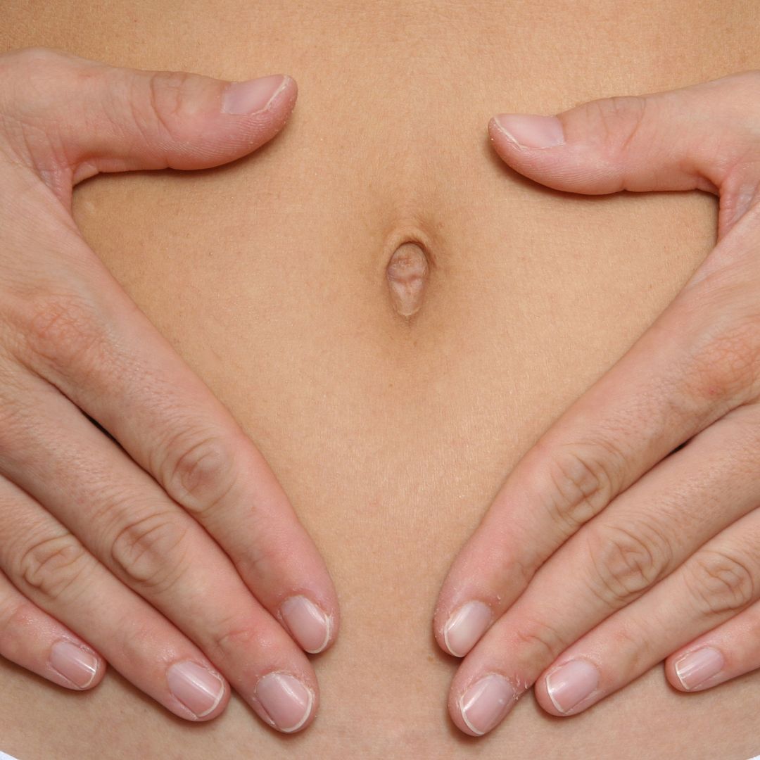 Close-up of a person's belly button with hands forming a heart shape around it.
