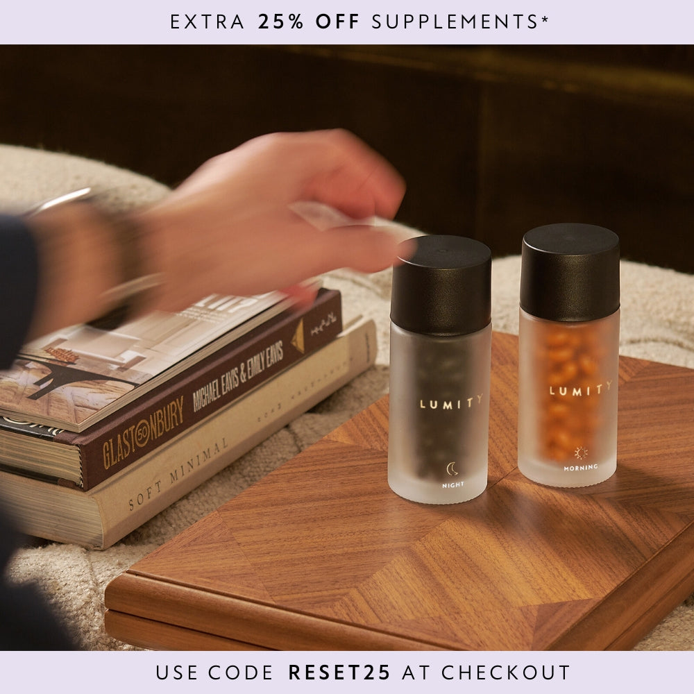 Two LUMITY bottles on a wooden table with books and hand reaching forward.