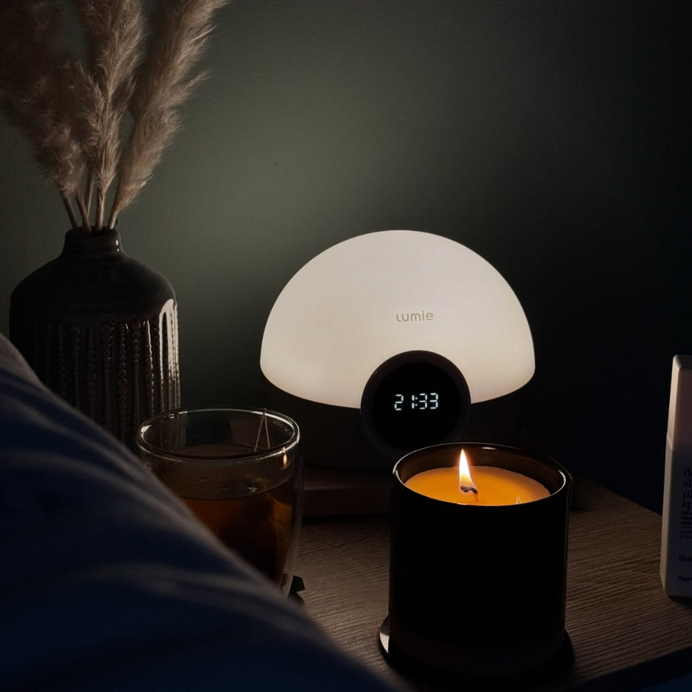 Image of Lumie alarm clock at night, ona bedside table next to a it candle, glass of water and dried foliage