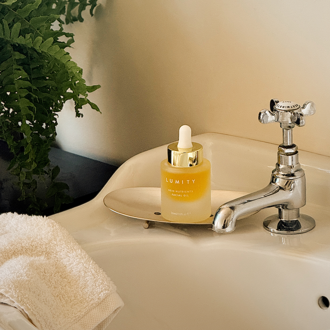 Lumity Facial Oil bottle on a bathroom sink with a plant in the background