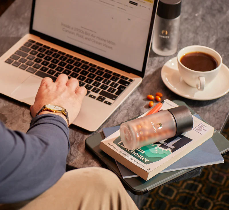 Photo of man working on his laptop at a desk with books, coffee and the Morning & Night supplement.
