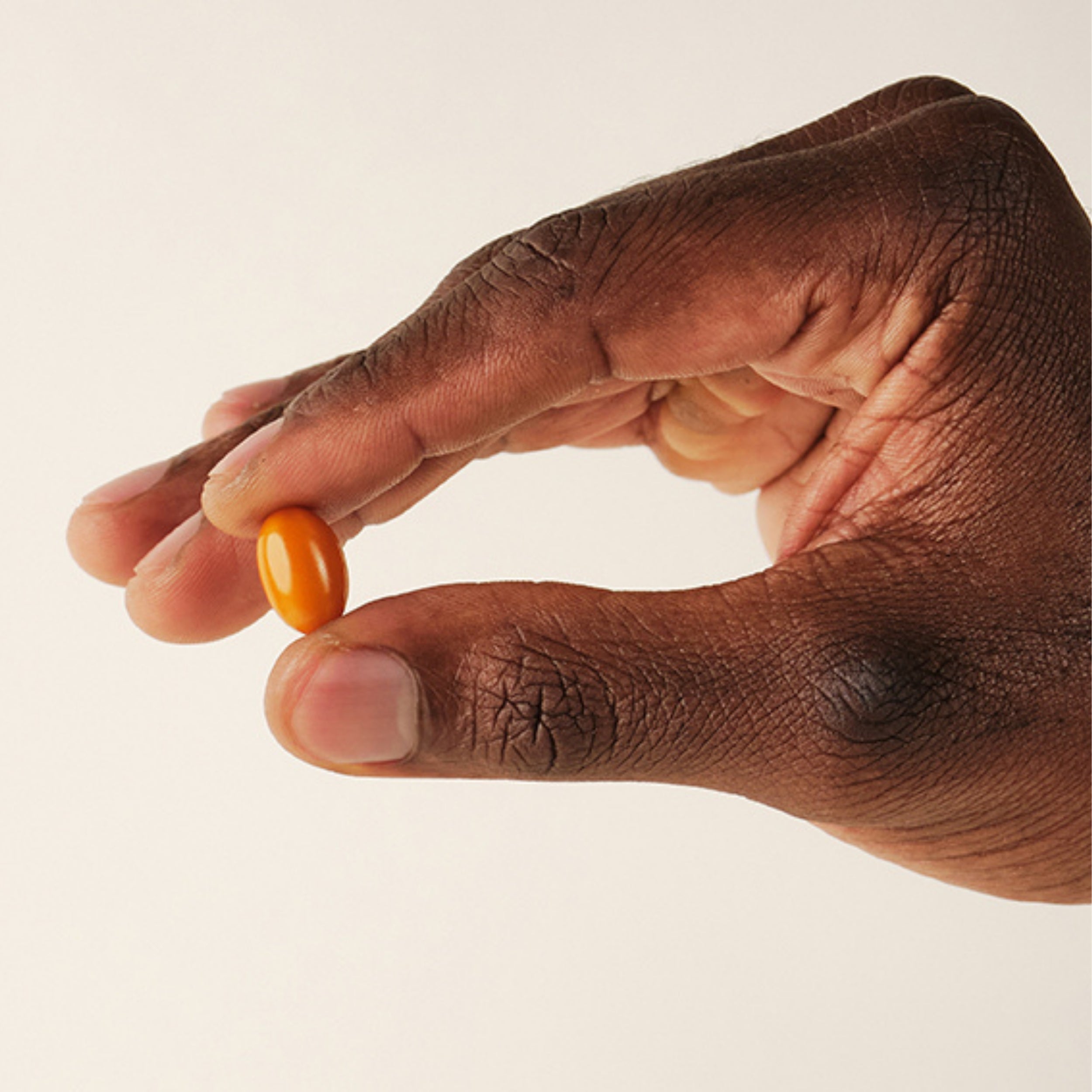 Hand holding an orange Lumity Morning Softgel against a beige background