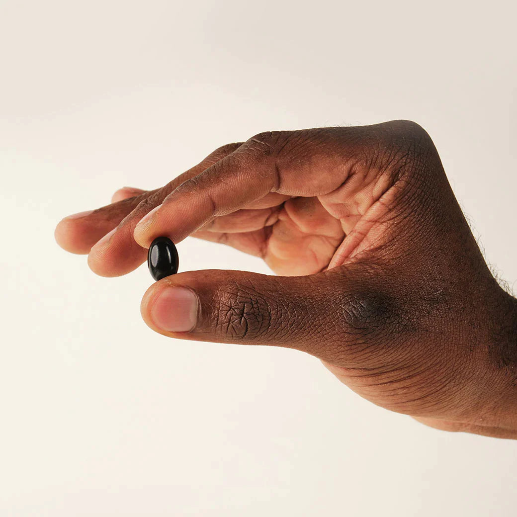 Hand holding a single smooth black softgel for men's antioxidant and cellular support in a daily wellness routine