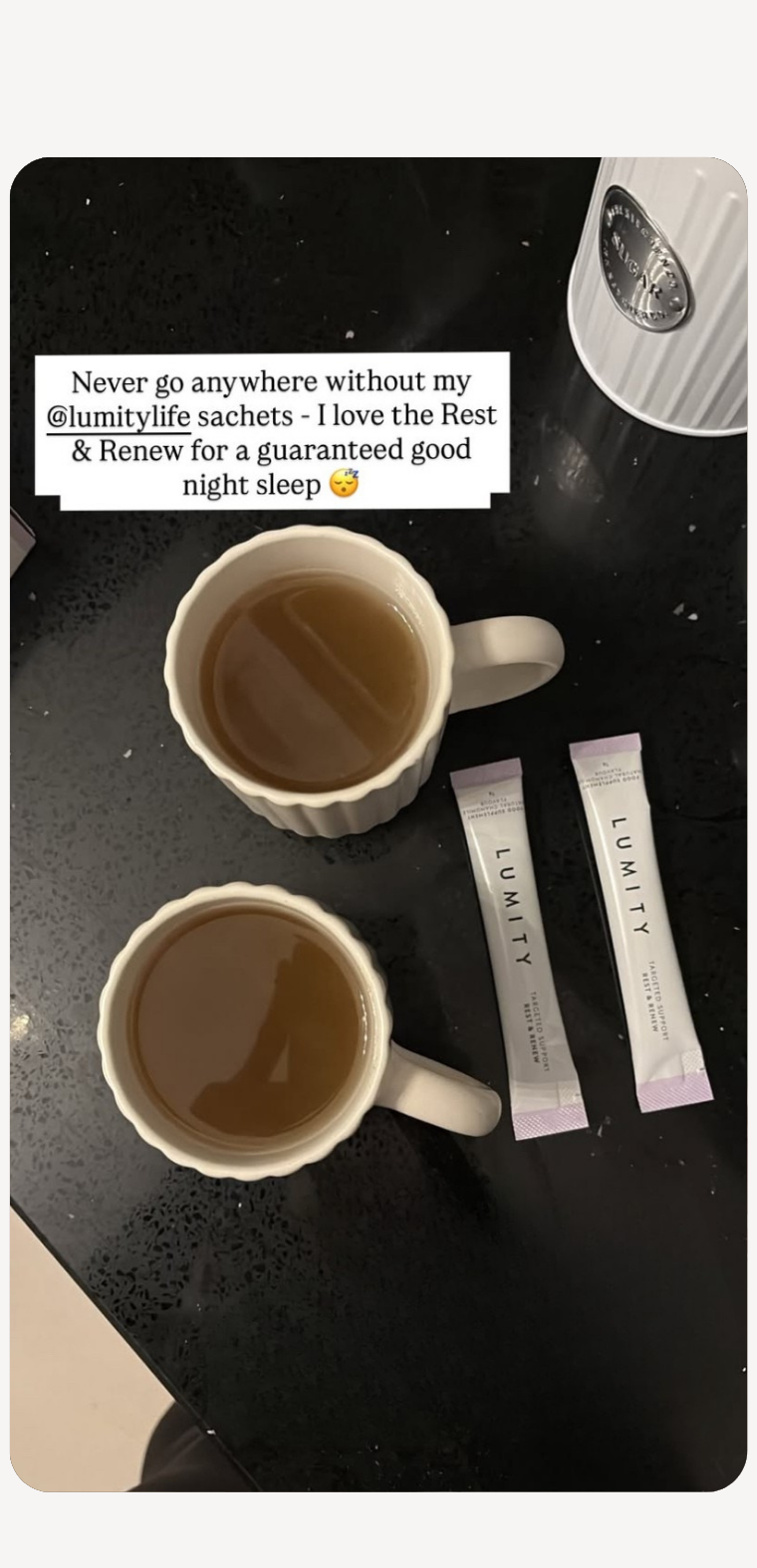 Two white mugs filled with tea beside two Lumity Rest & Renew sachets on a dark countertop with a white container nearby