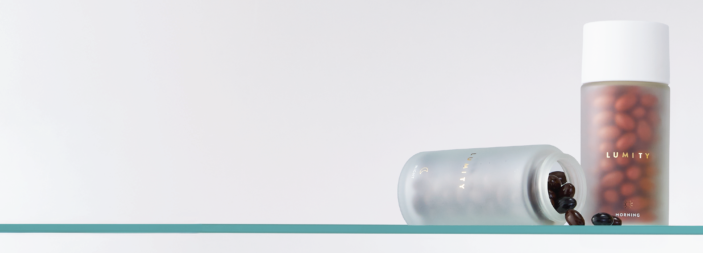 Two frosted Lumity bottles with dark soft spheres, one standing upright and one lying down on a glass shelf with soft lighting