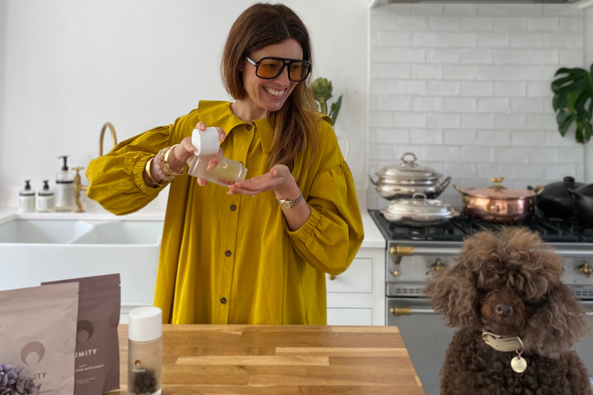 Woman taking Morning supplement next to her dog in kitchen