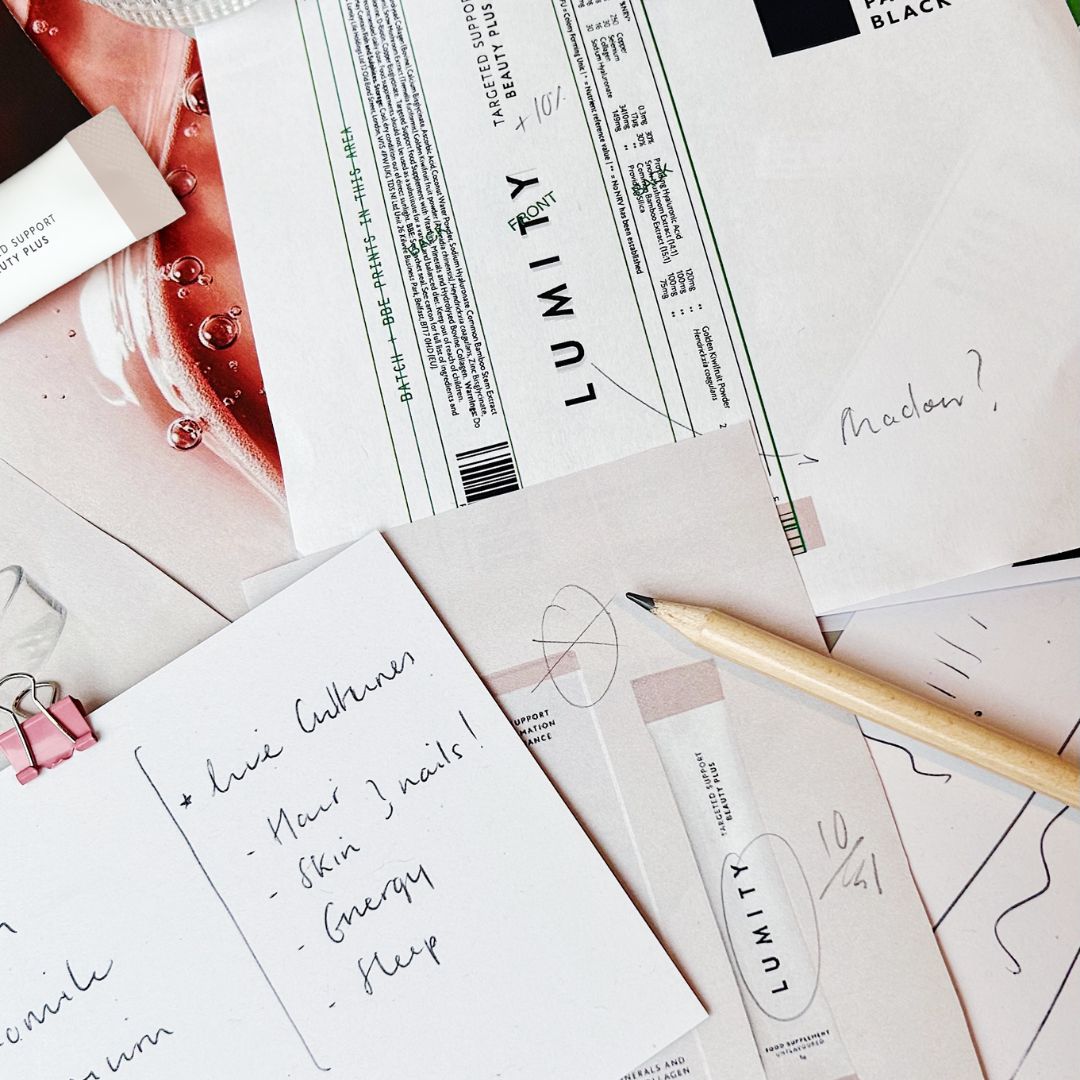 Flat lay of handwritten notes, Lumity supplement packaging sketches, and a pencil on a white surface