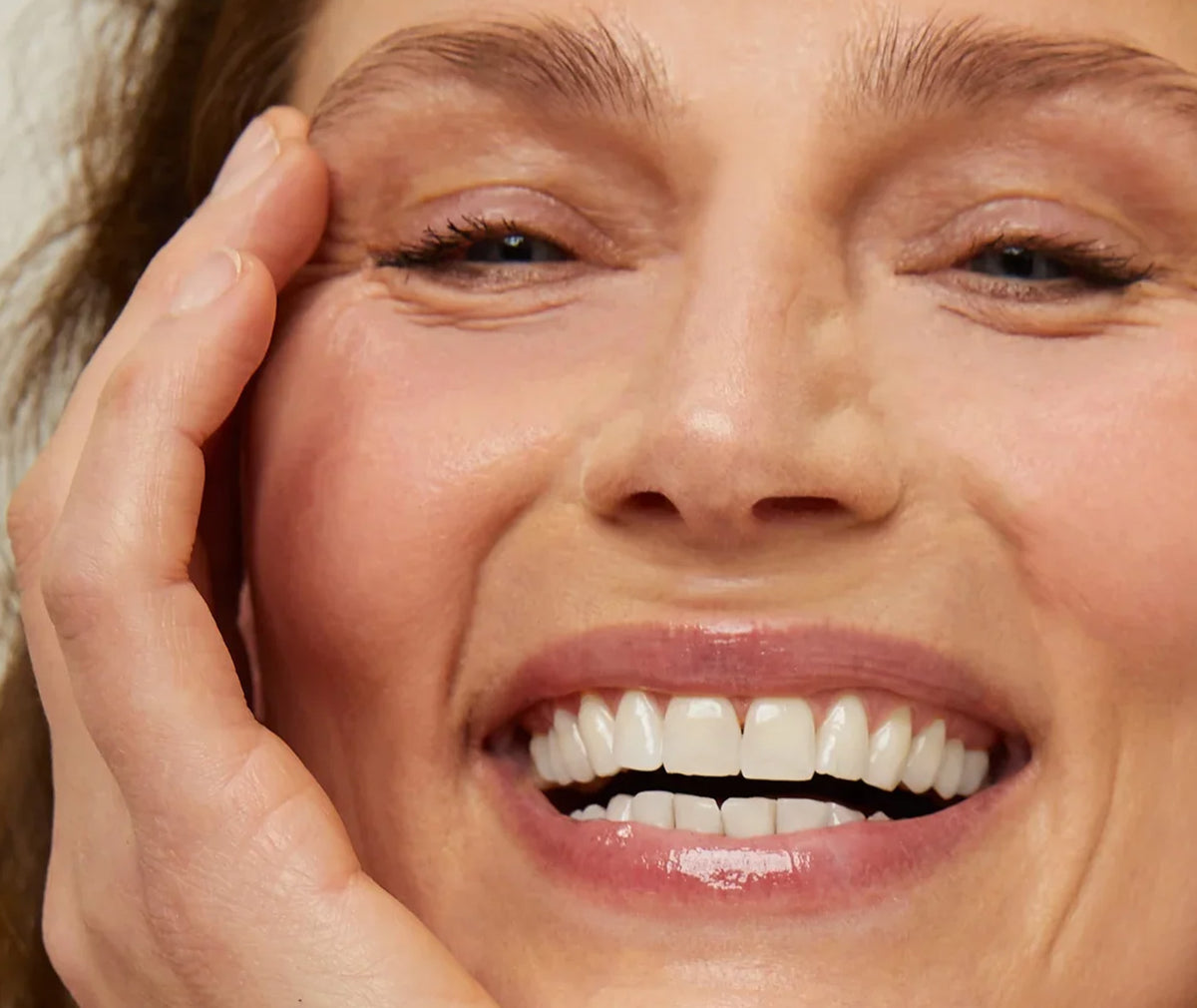 Close-up of a joyful person smiling with natural skin texture and a hand gently resting on their face.