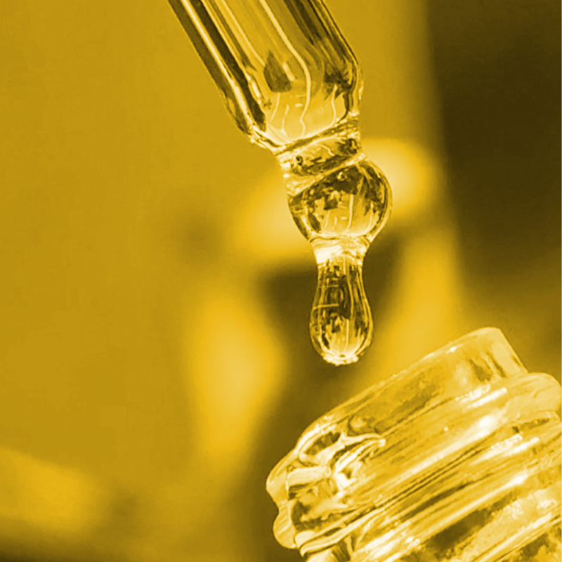Close-up of a Lumity Skin Nutrients Body Oil pipette dropper with oil being dispensed against a yellow background