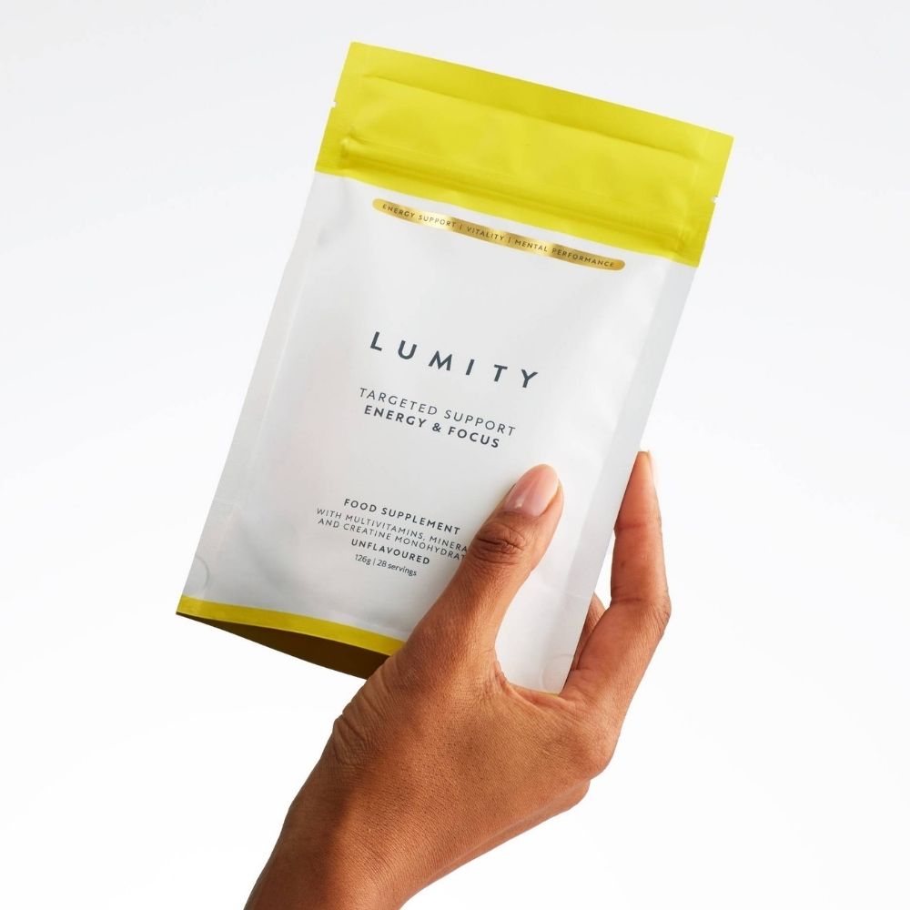 Hand holding a matte white and yellow pouch of Lumity's energy support supplement for daily wellbeing