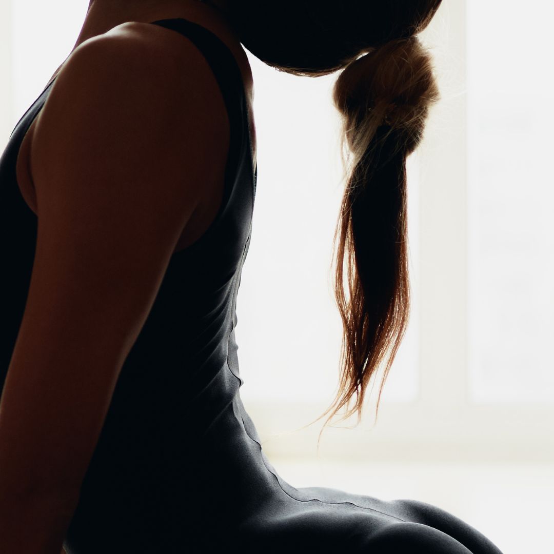Woman stretching, wearing a dark tank top on a blurred background