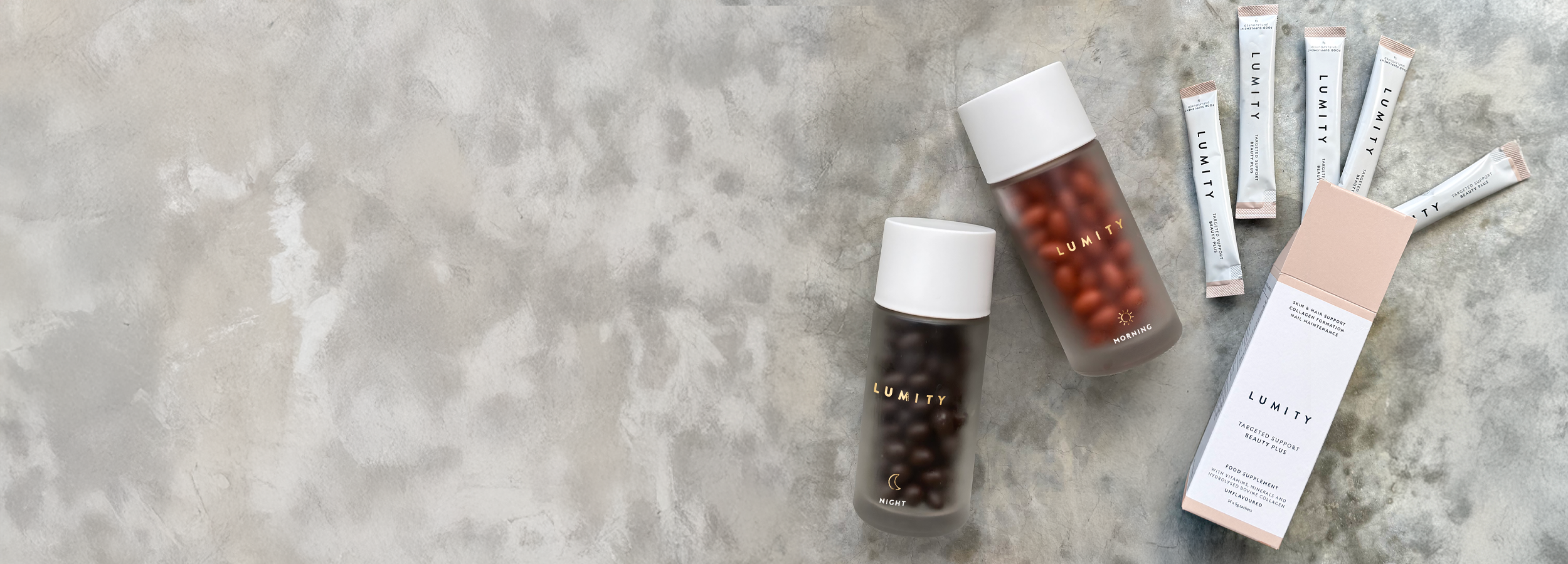 Two frosted Lumity Life bottles with brown and amber beads next to sachets and a soft pink box on a neutral surface