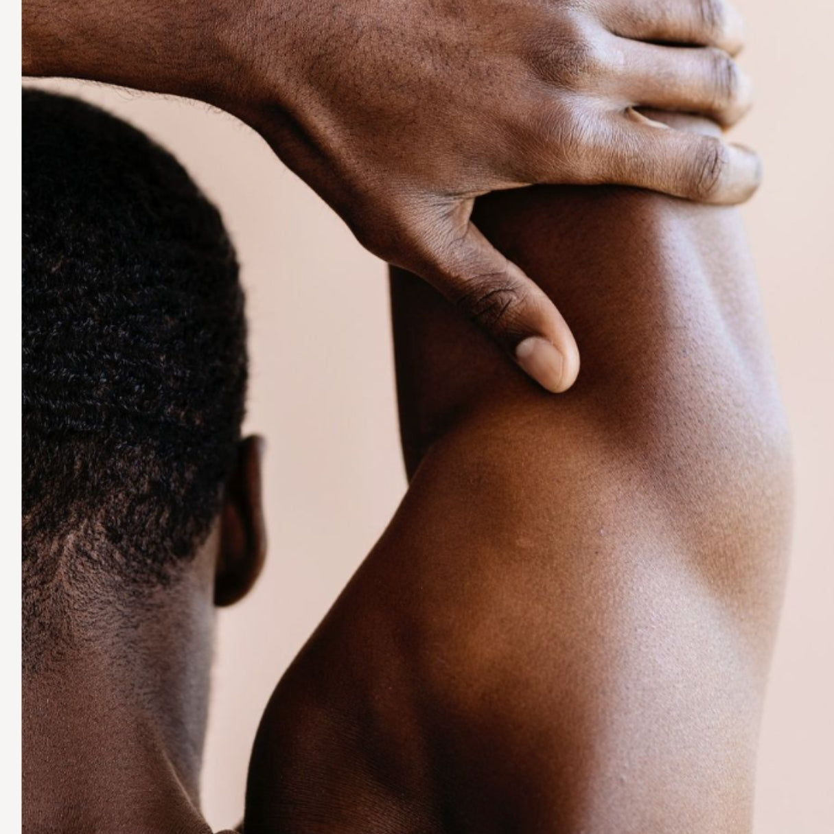 Close-up of a male hand resting on a shoulder against a neutral background

