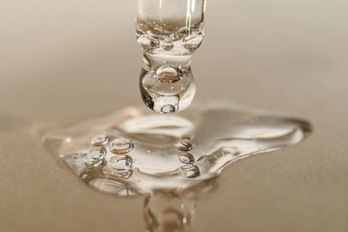 Close-up of a pipette dripping water on a reflective surface.