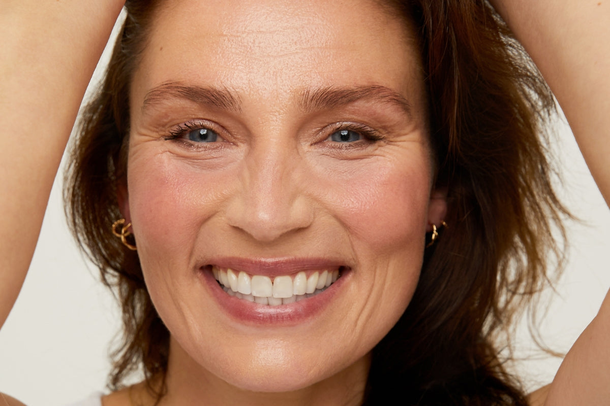 Close-up of a woman with a bright smile and jewellery against a neutral background